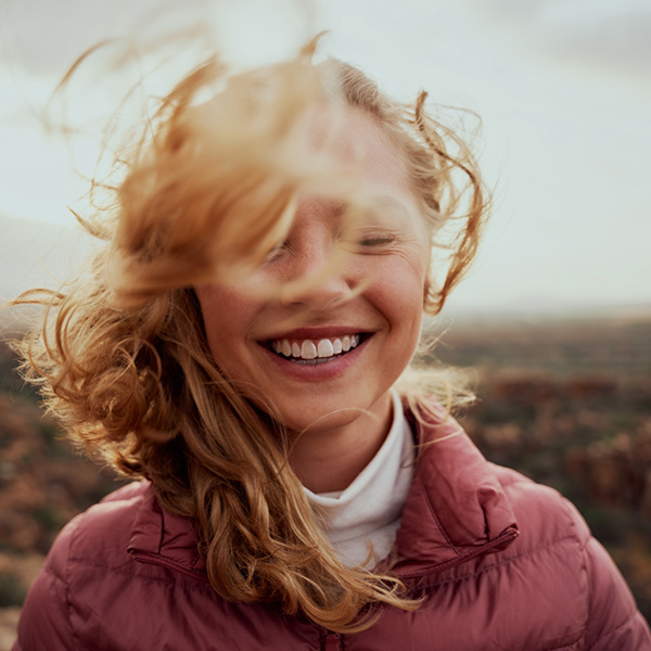 Portrait of young smiling woman face partially covered with flying hair in windy day